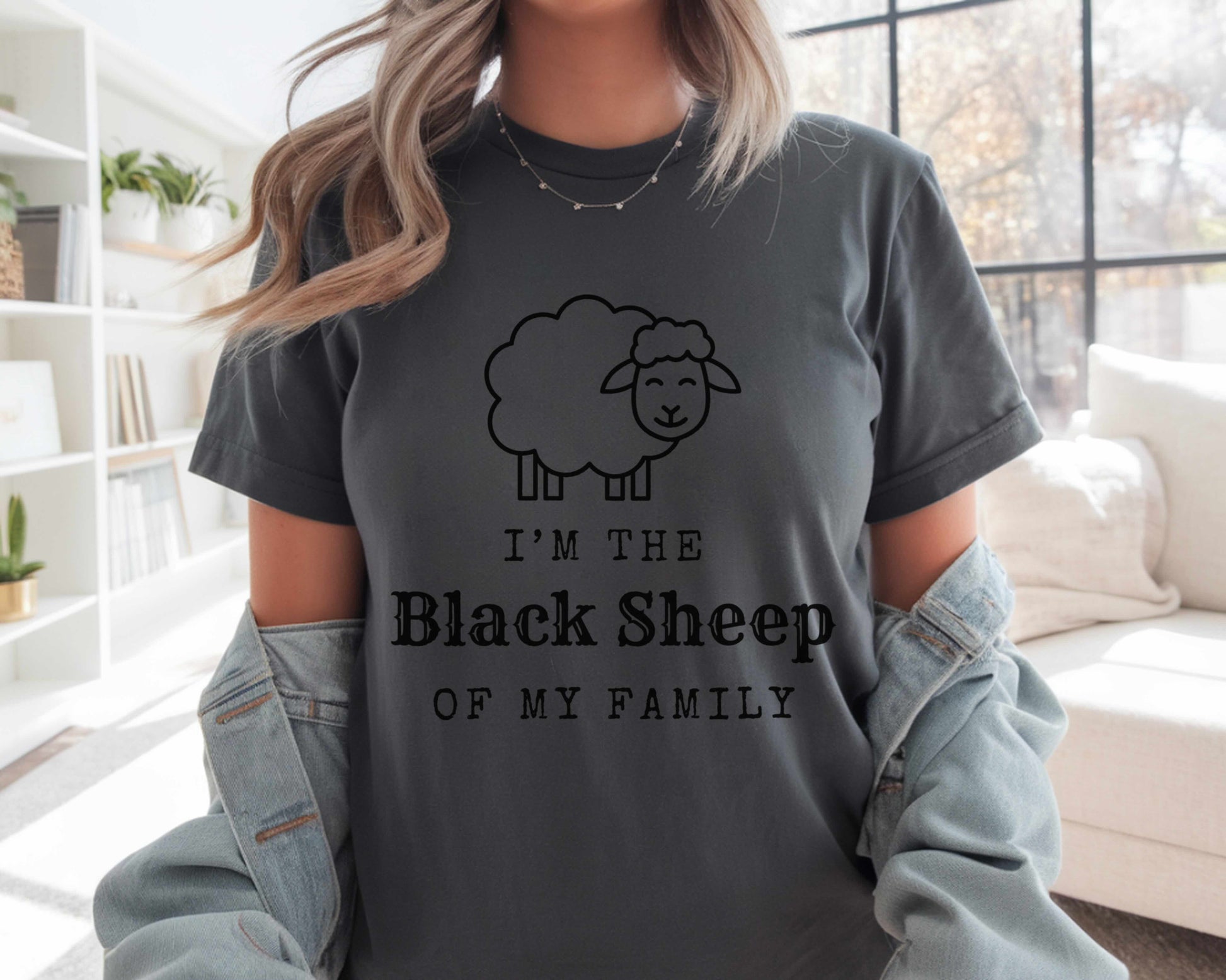 Person wearing a dark gray t-shirt with  'I'm the Black Sheep of My Family' design in a living room.