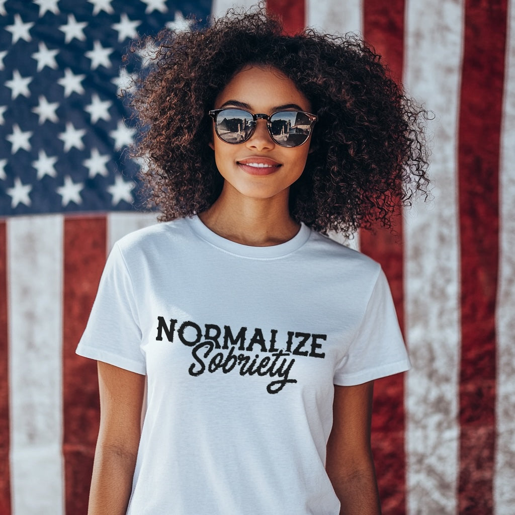 Person wearing a white t-shirt with 'NORMALIZE Sobriety' text in front of an American flag.