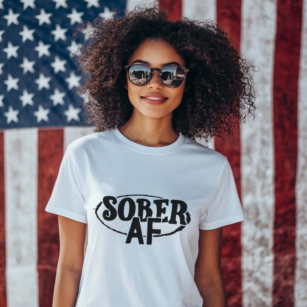 Person wearing a white t-shirt with 'SOBER AF' text in front of an American flag.