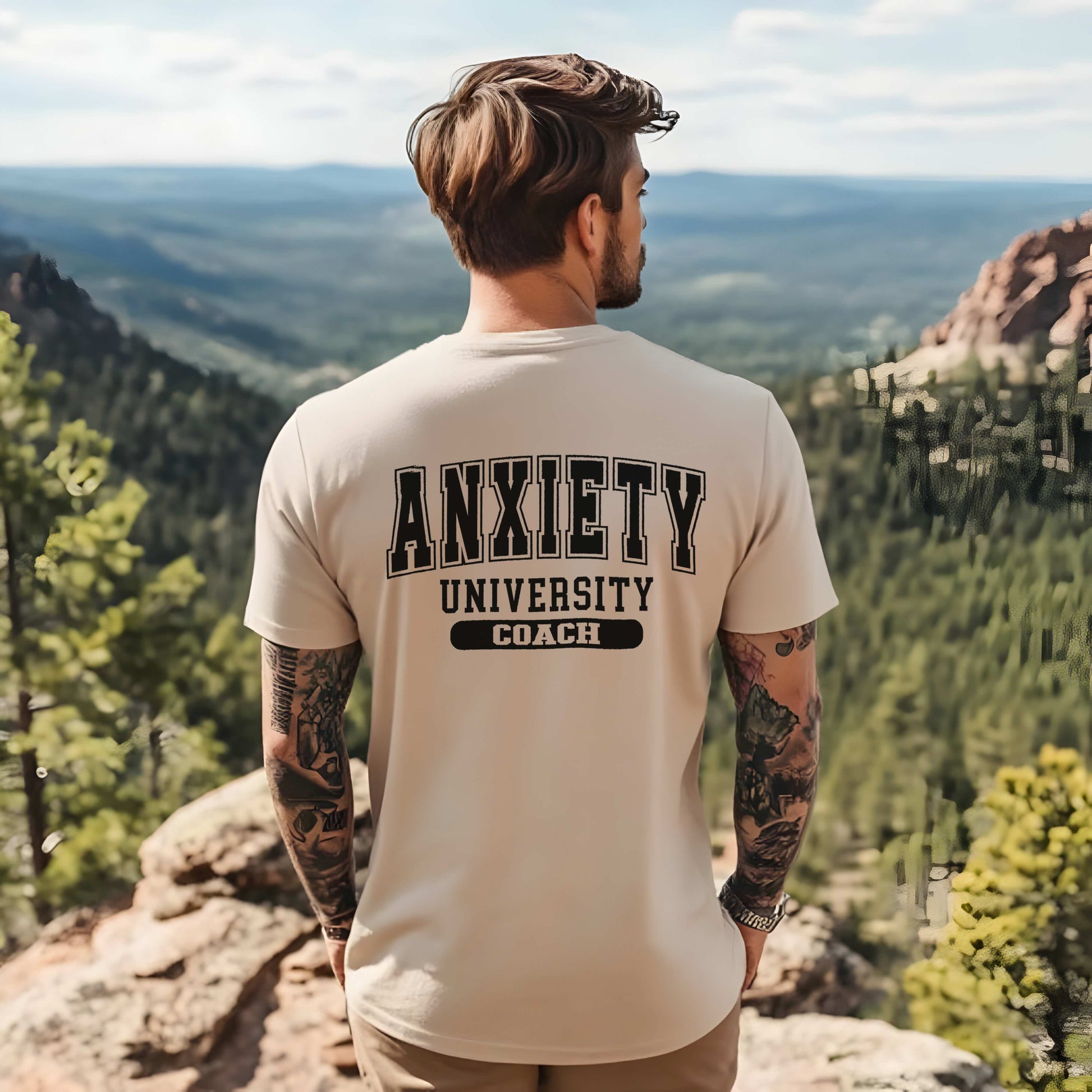 Person wearing a t-shirt with 'Anxiety University Coach' text, standing on a mountain overlooking a scenic landscape.