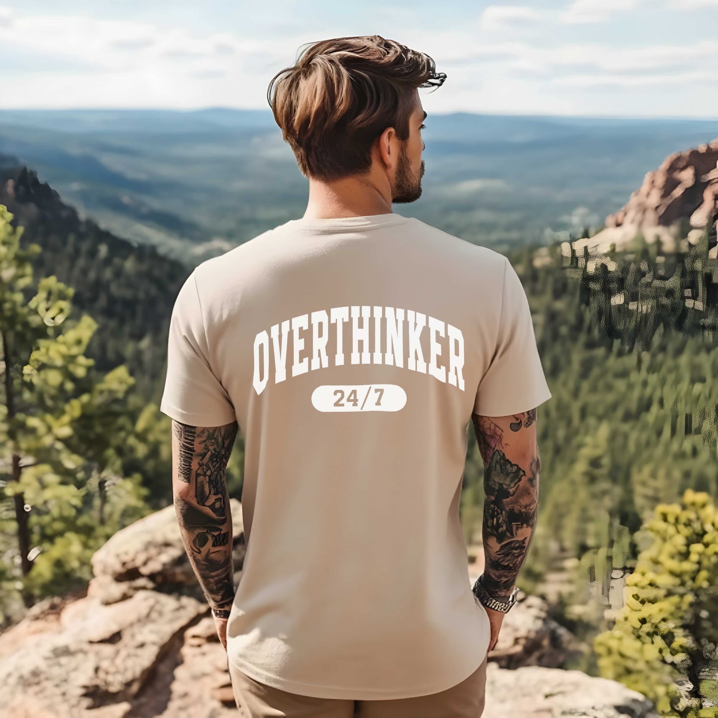 Man wearing a 'OVERTHINKER 24/7' t-shirt overlooking a scenic landscape.
