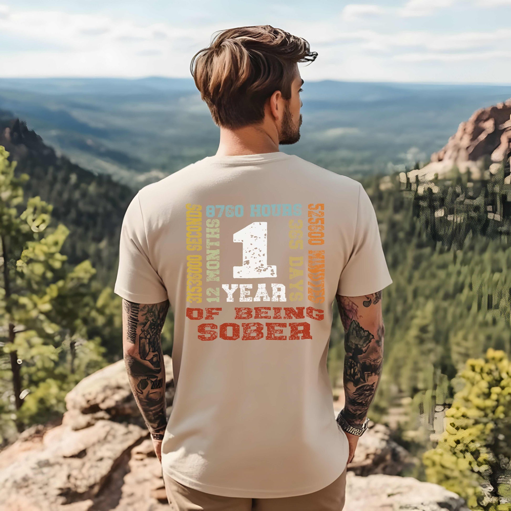 Man wearing a t-shirt celebrating one year of sobriety, standing on a scenic overlook.