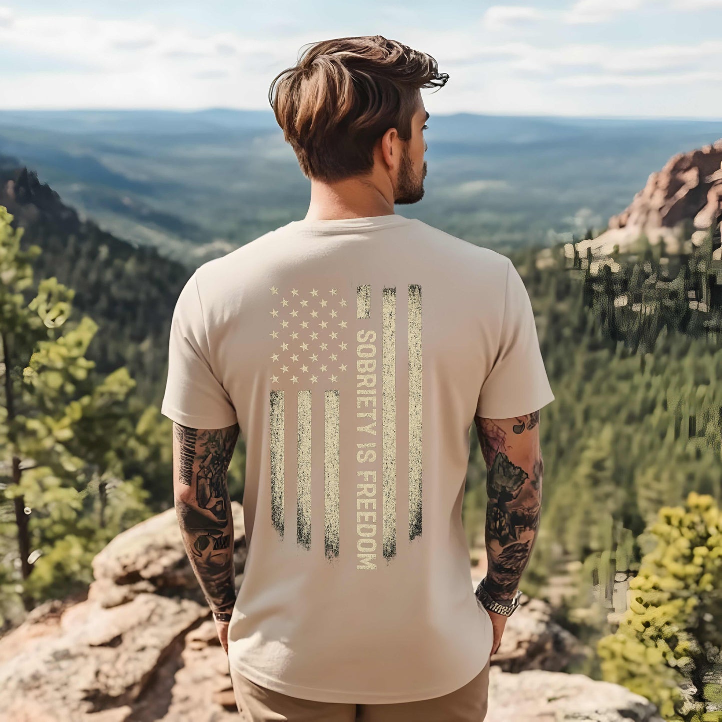 Man wearing a t-shirt with 'Sobriety is Freedom' design, standing on a mountain overlooking a scenic landscape.
