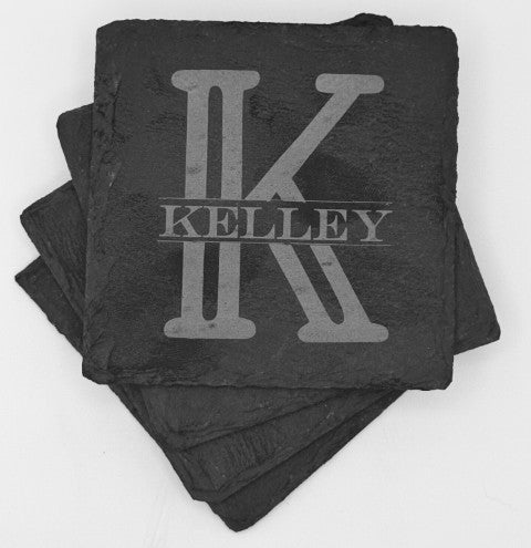 A set of four stacked slate black square coasters with an engraved design. The top coaster features a large, bold letter monogram and the last name horizontally across the middle of the monogram. The engraving is a lighter shade, creating contrast against the dark background of the coaster.