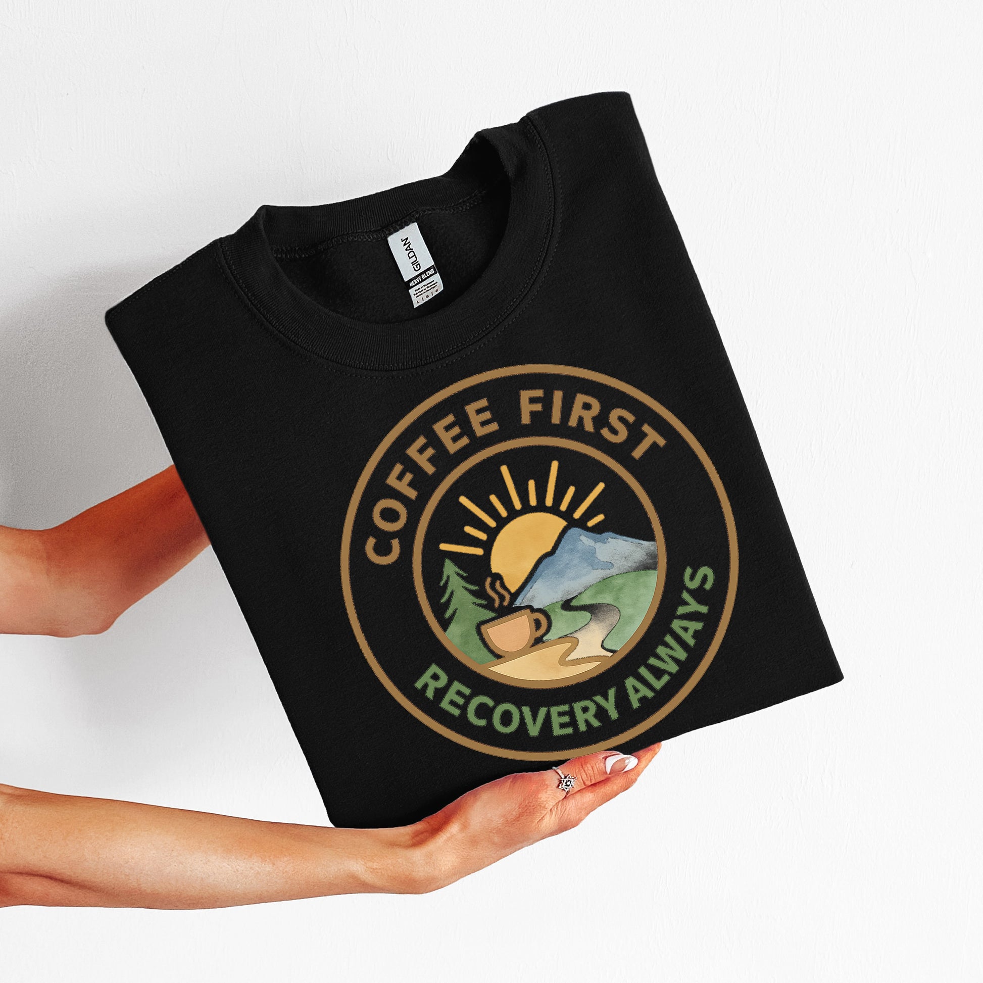 Black t-shirt with 'Coffee First, Recovery Always' design held by a person on a white background