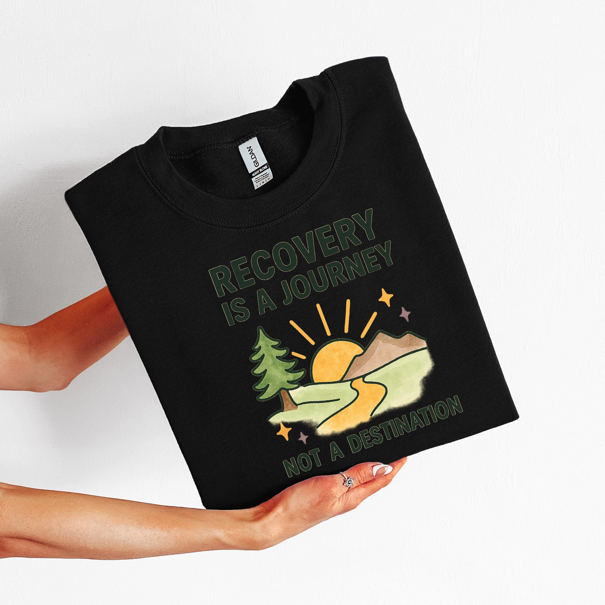 Black t-shirt with 'Recovery is a Journey, Not a Destination' graphic held by a person on a white background