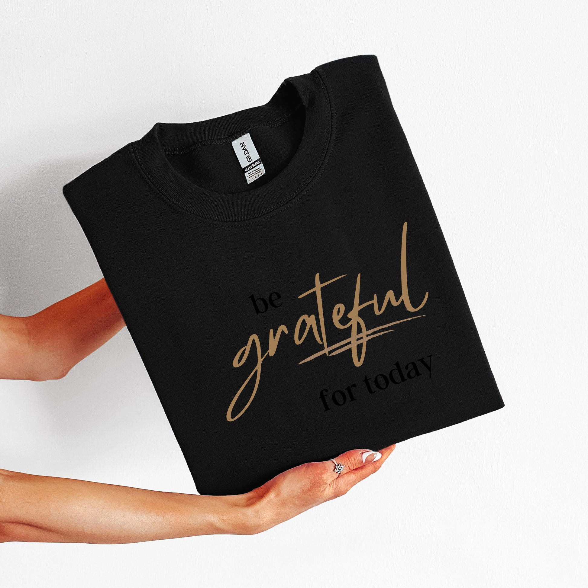 Black t-shirt with 'be grateful for today' text held by a person on a white background