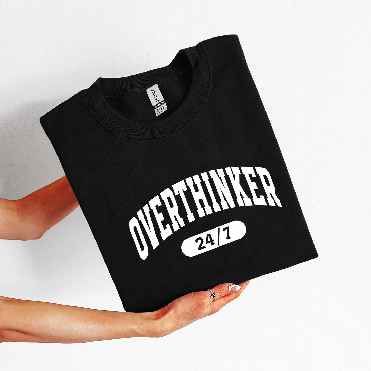 Black t-shirt with 'OVERTHINKER 24/7' text held by a person on a white background