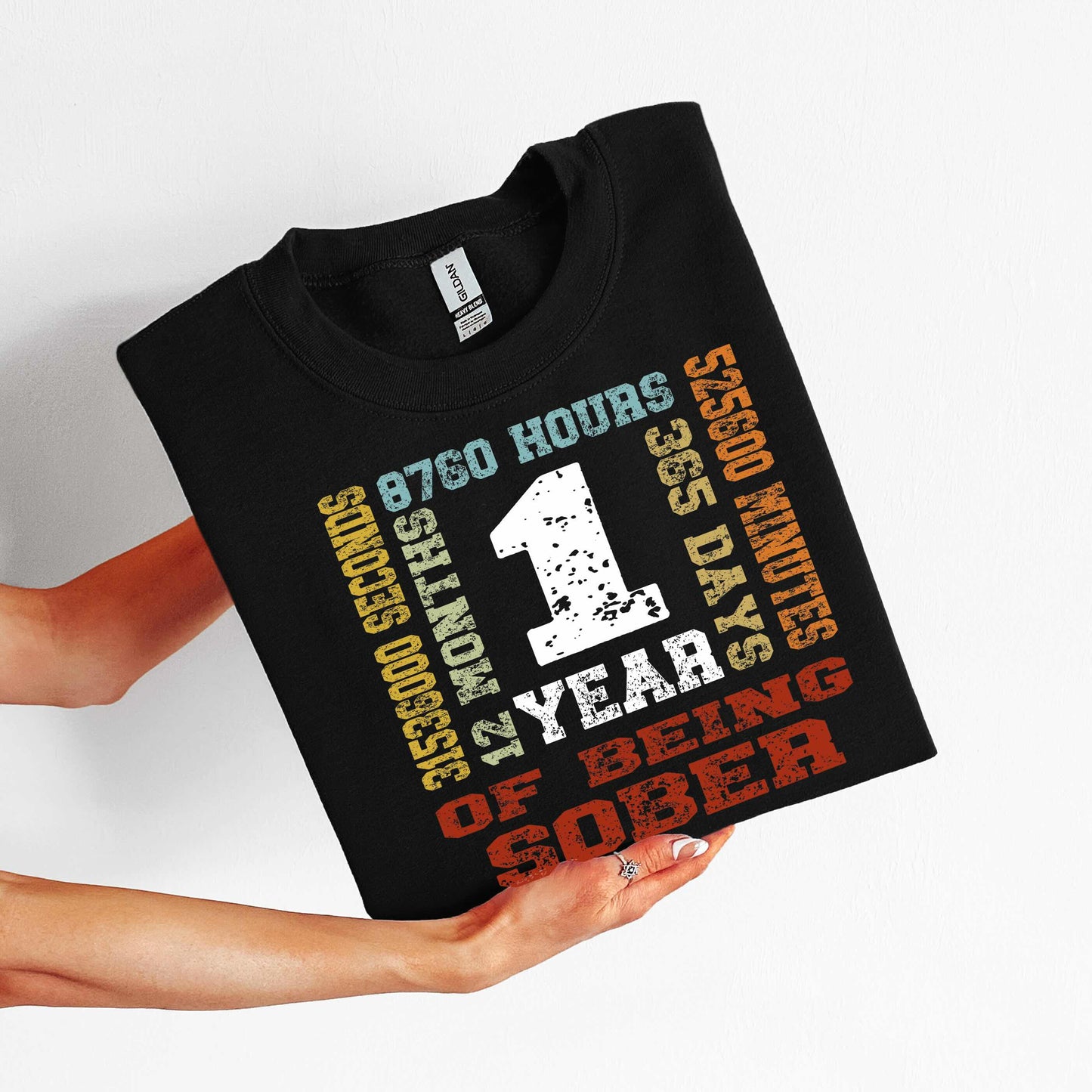 Black t-shirt with colorful '1 year sober' design held by a person on a white background