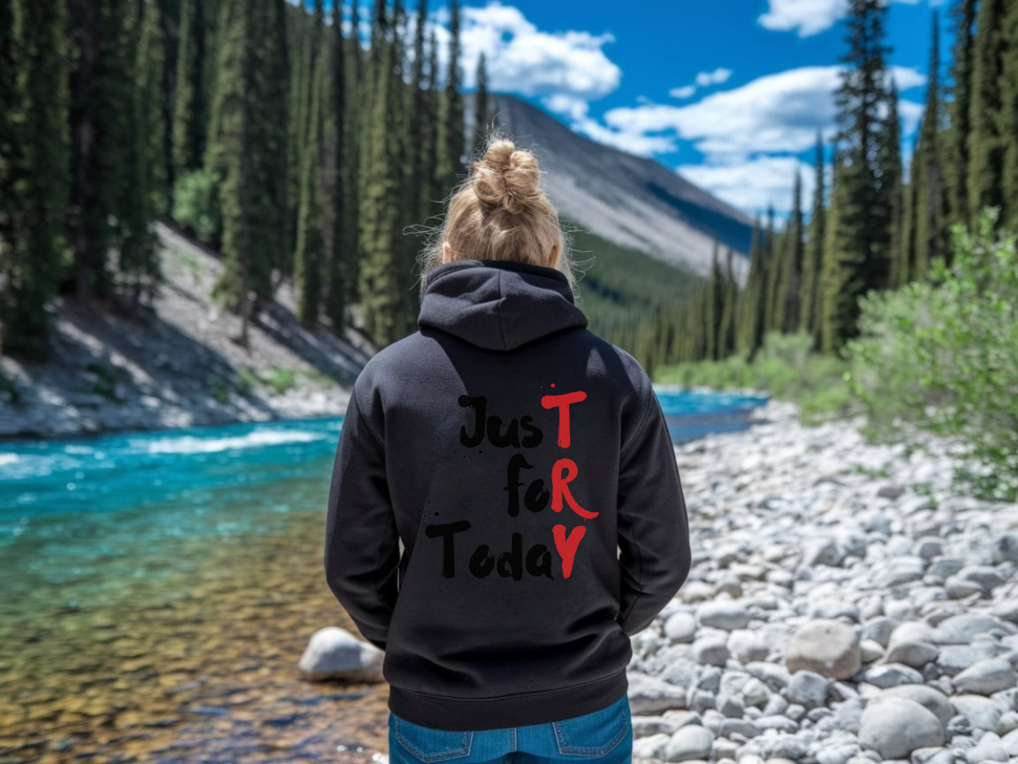 Person wearing a black hoodie with text standing by a river and forest