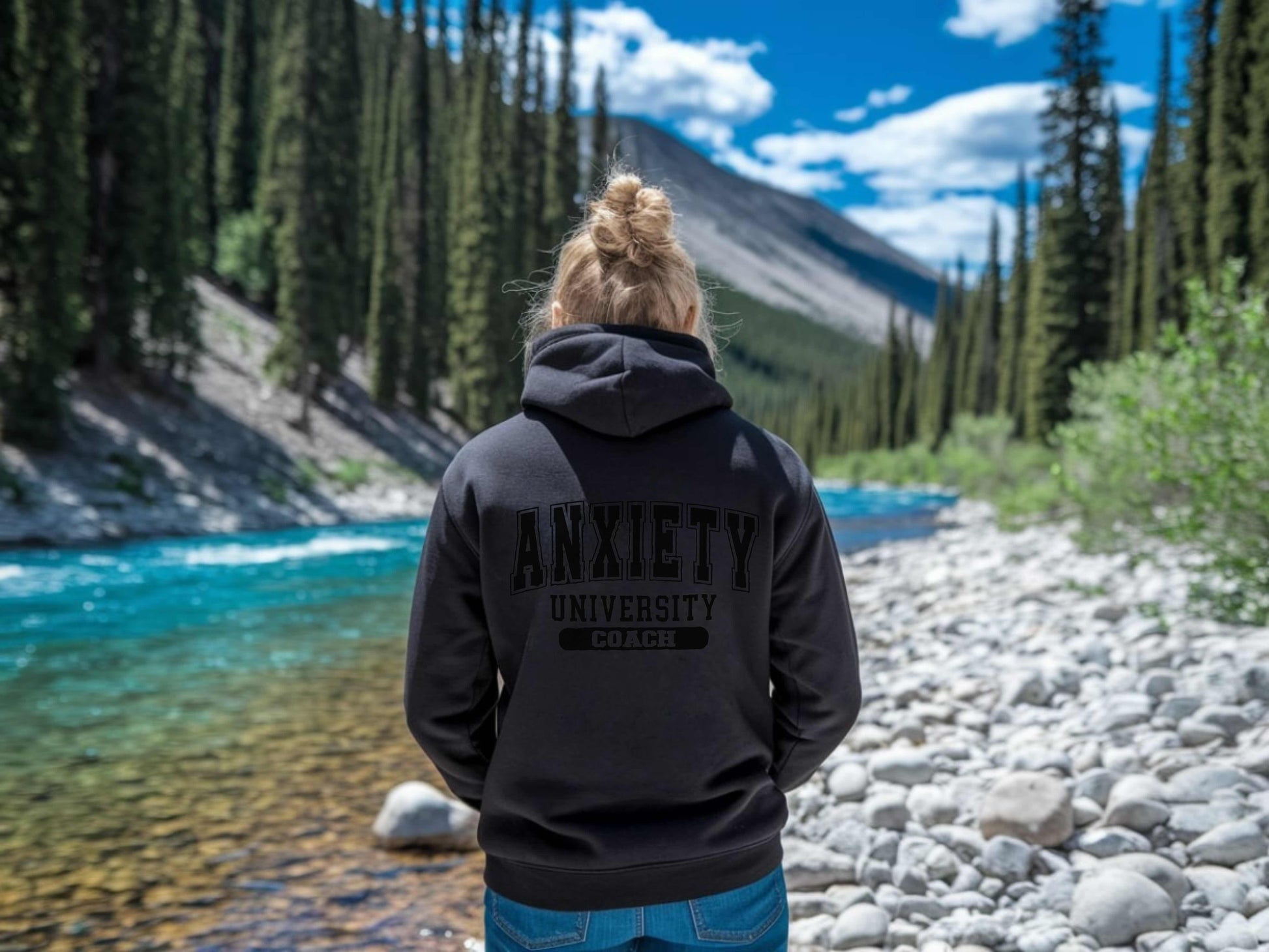 Person wearing a black hoodie with 'ANXIETY UNIVERSITY' text in a natural setting.