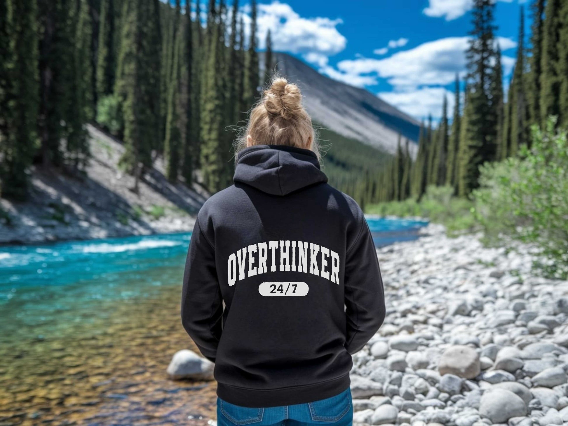 Person wearing a black hoodie with 'OVERTHINKER 24/7' text in a natural setting.