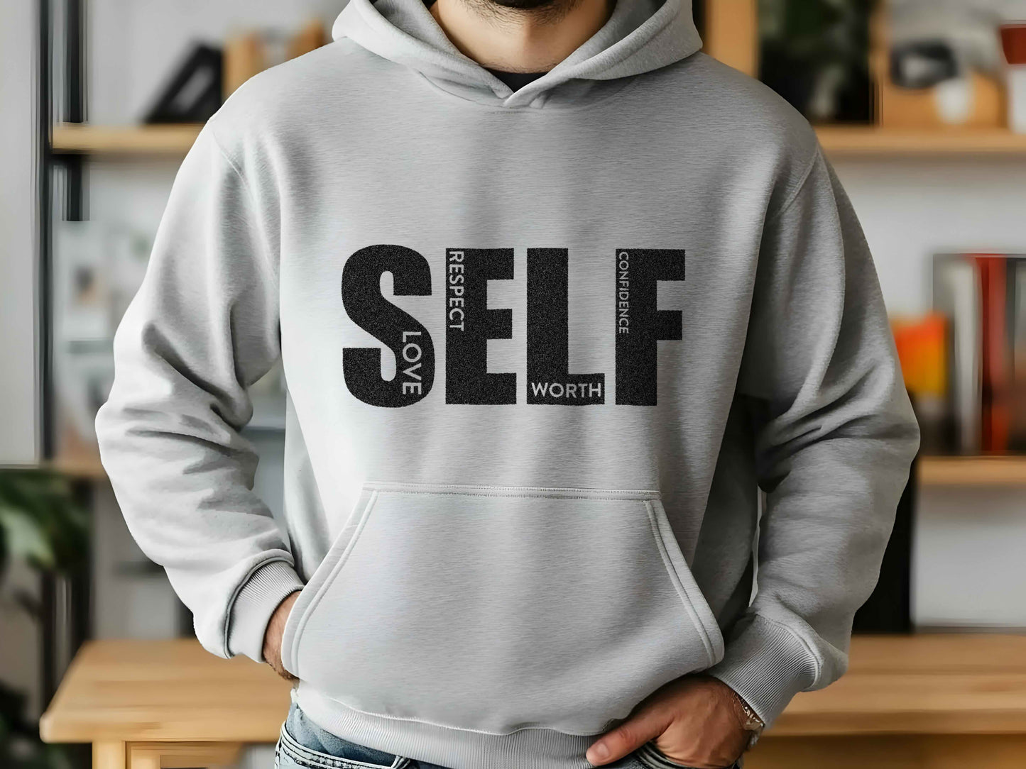 Person wearing a gray hoodie with 'SELF love respect worth confidence' text in a casual indoor setting