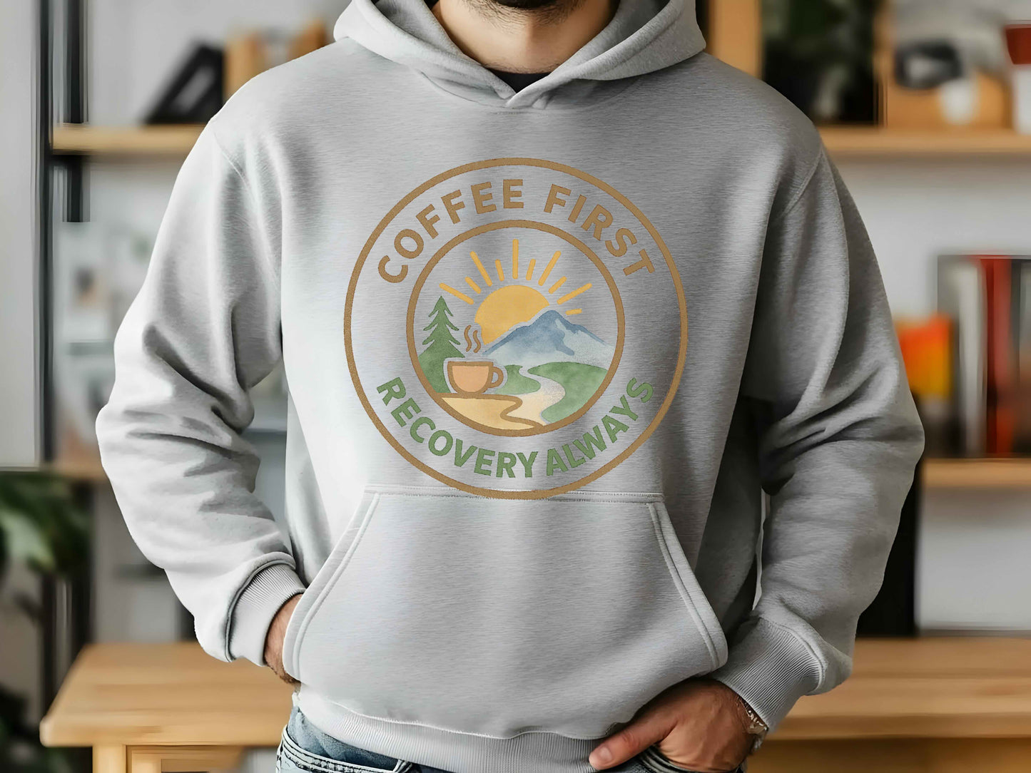 Person wearing a gray hoodie with a 'Coffee First, Recovery Always' graphic design.