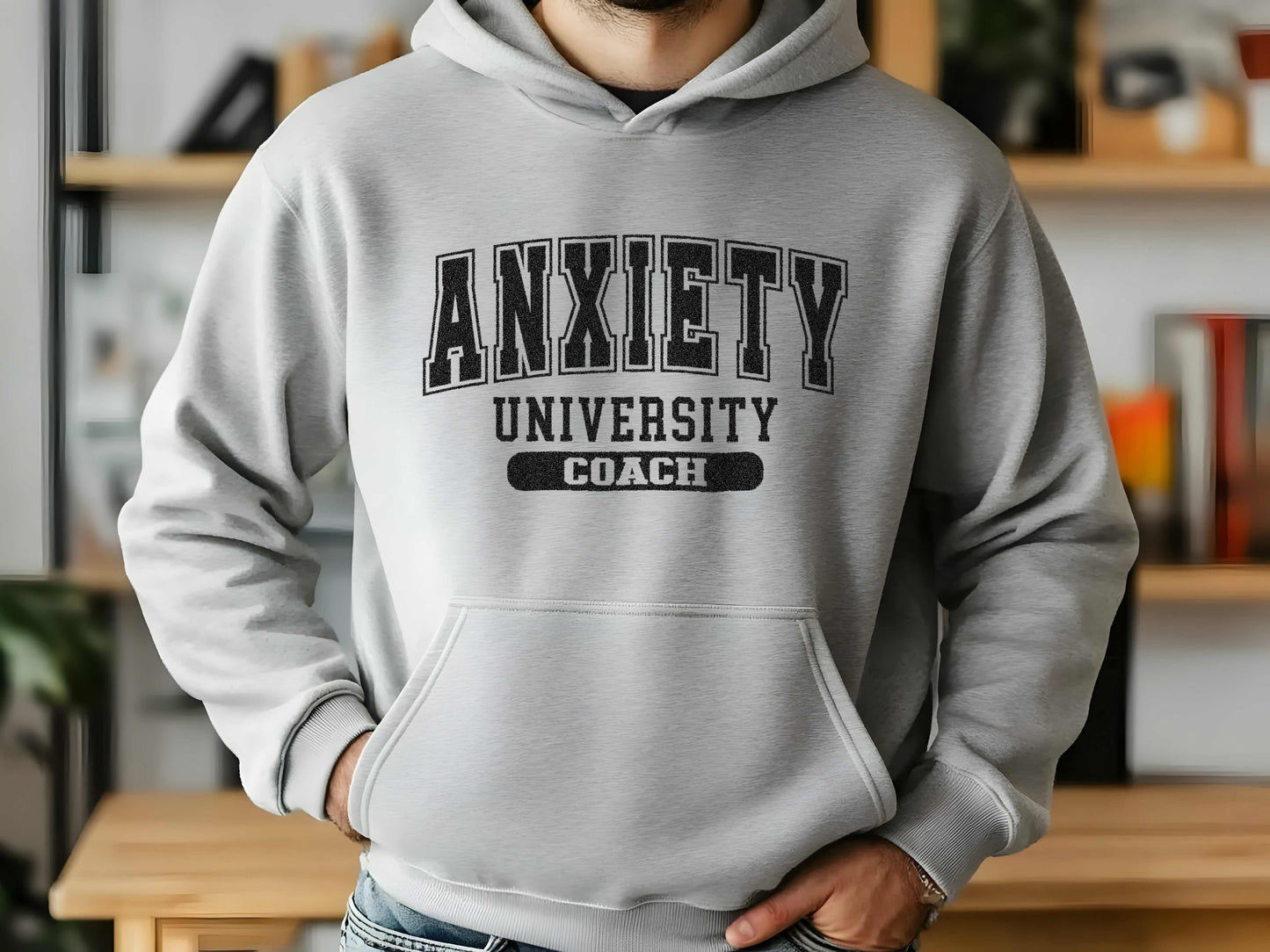 Person wearing a gray hoodie with 'Anxiety University Coach' text in a casual setting.