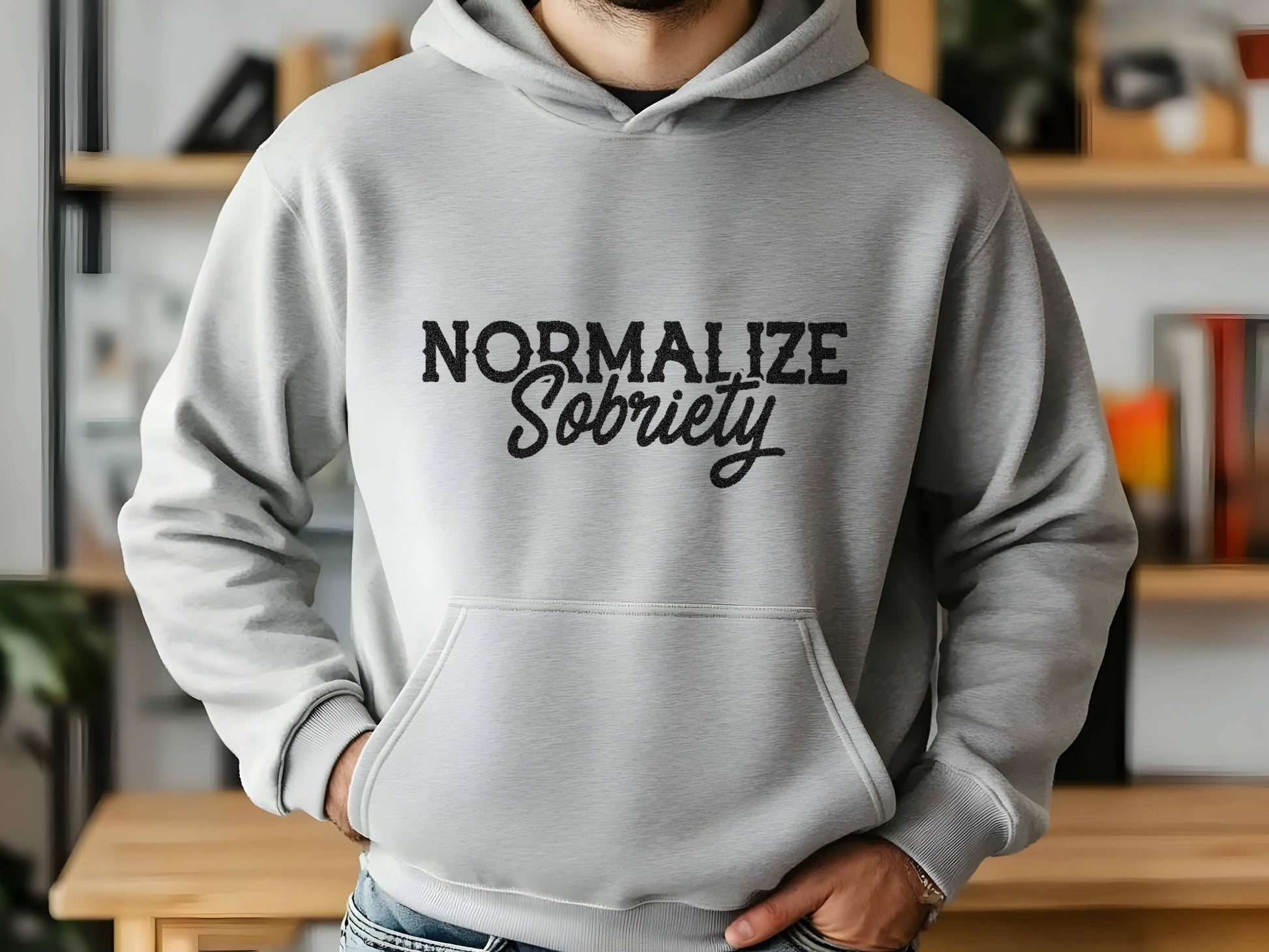 Person wearing a gray hoodie with 'Normalize Sobriety' text in a casual setting.