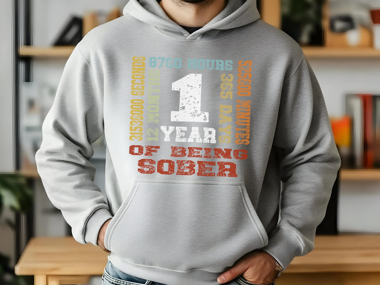 Person wearing a gray hoodie with '1 year sober' design, standing indoors.