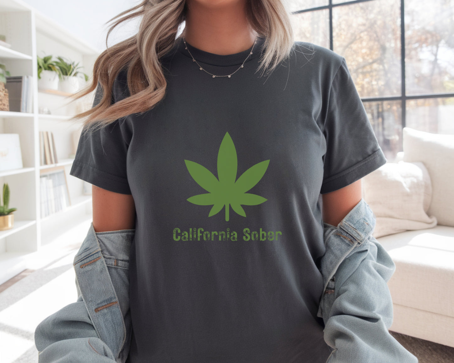 Person wearing a dark gray t-shirt with a green cannabis leaf design and 'California Sober' text in a living room.