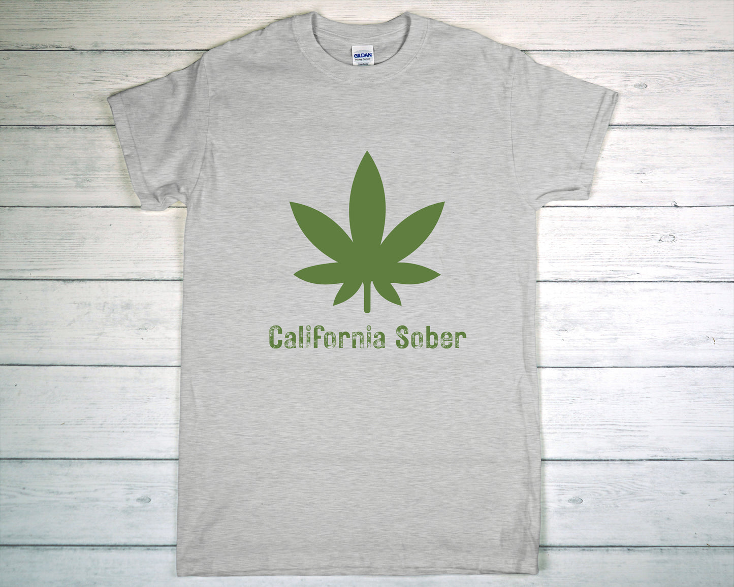Gray t-shirt with green cannabis leaf and 'California Sober' text on a wooden background