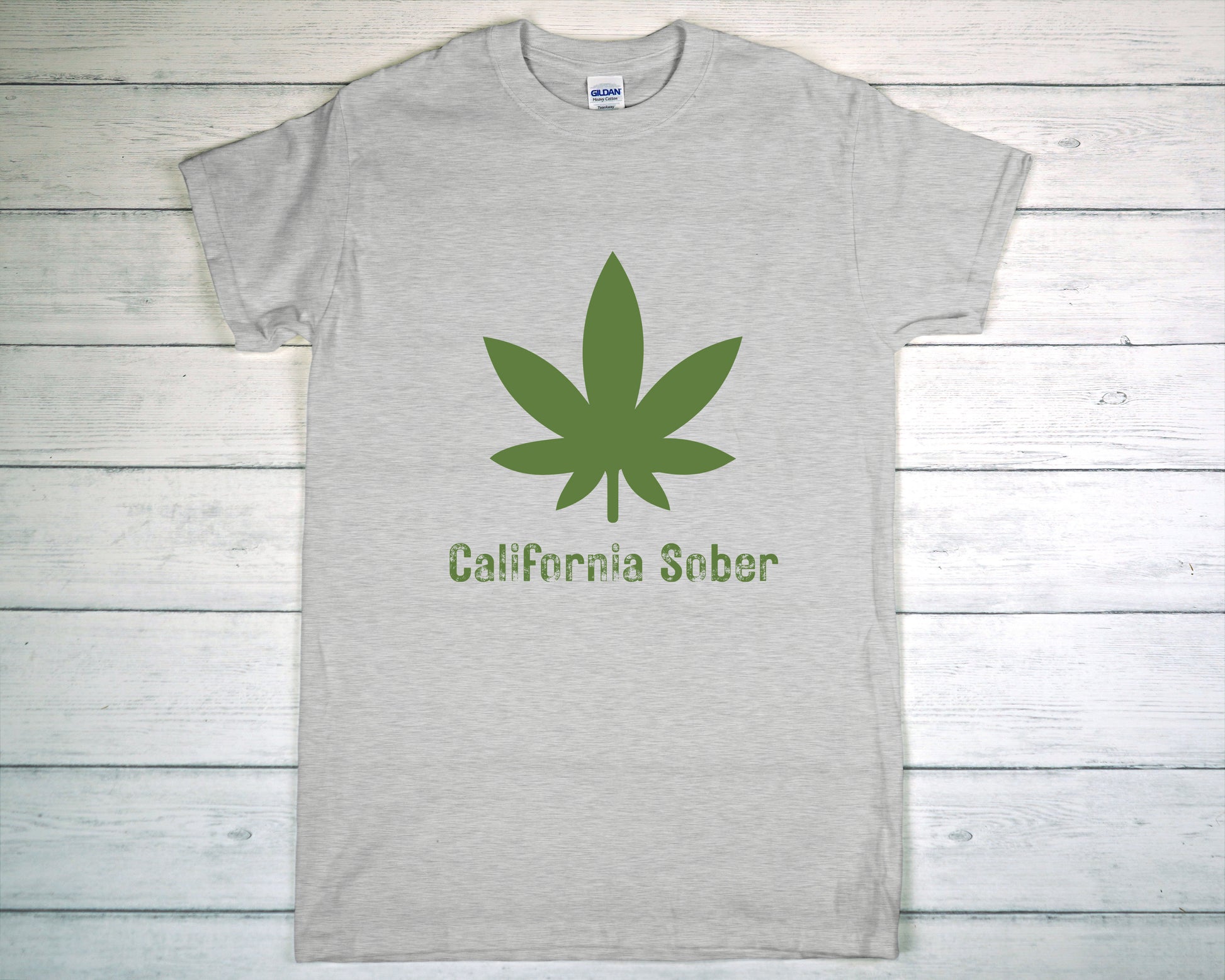 Gray t-shirt with green cannabis leaf and 'California Sober' text on a wooden background