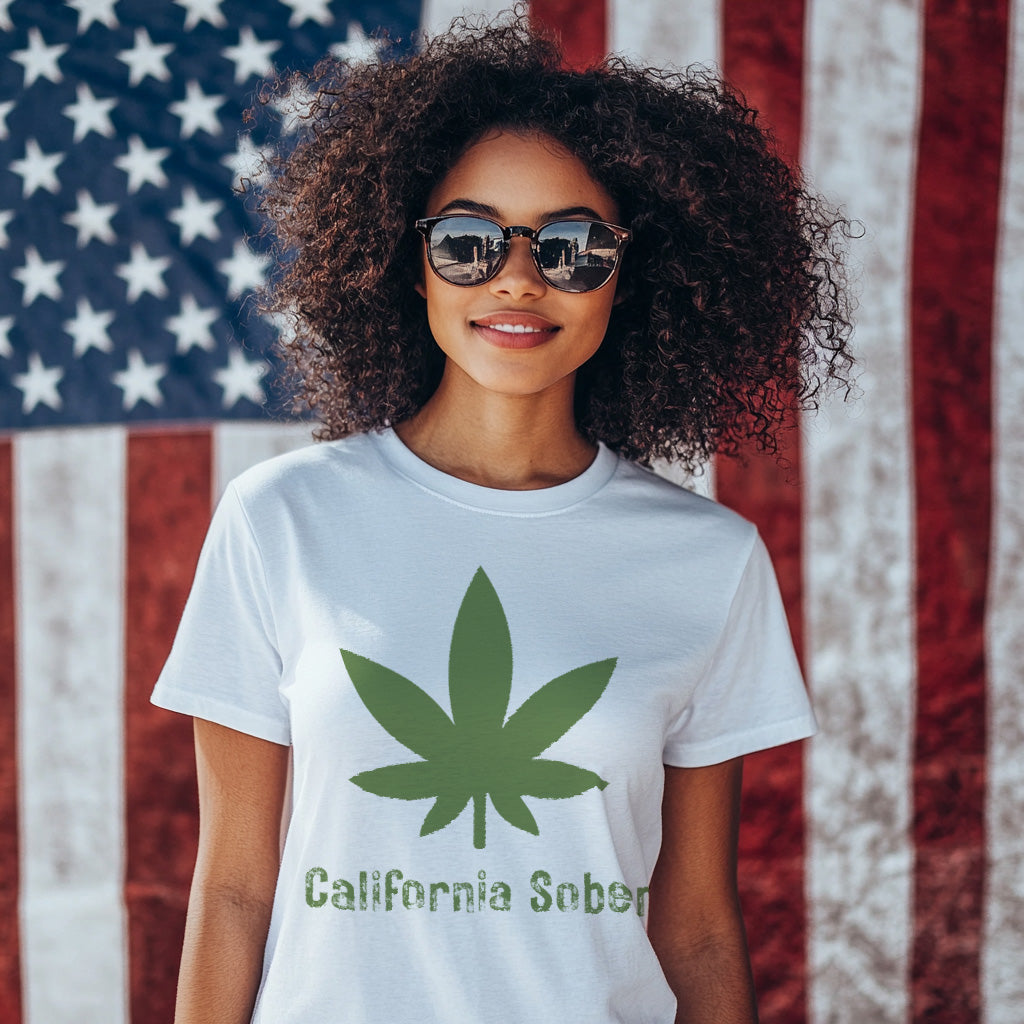 Person wearing a white t-shirt with a green cannabis leaf and 'California Sober' text in front of an American flag.