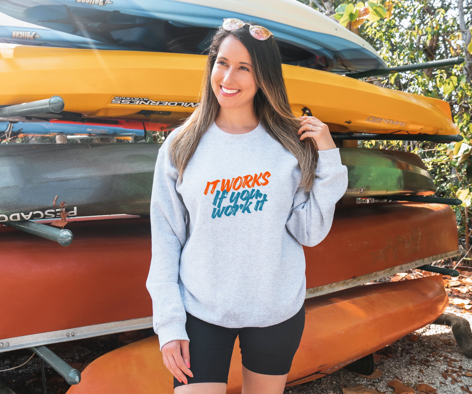 Woman wearing a sweatshirt with motivational text in front of stacked kayaks.