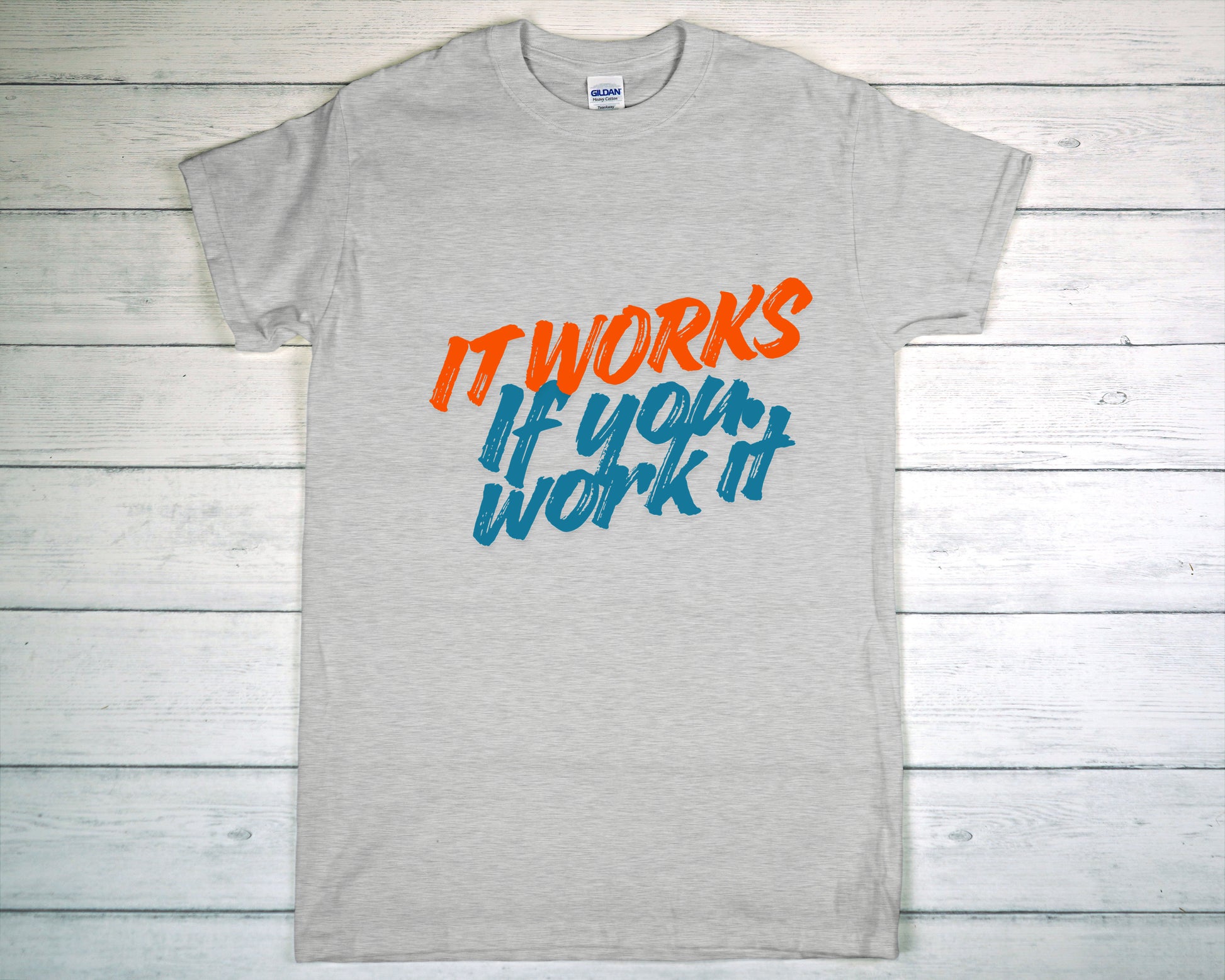 Gray t-shirt with motivational text 'It works if you work it' on a wooden background