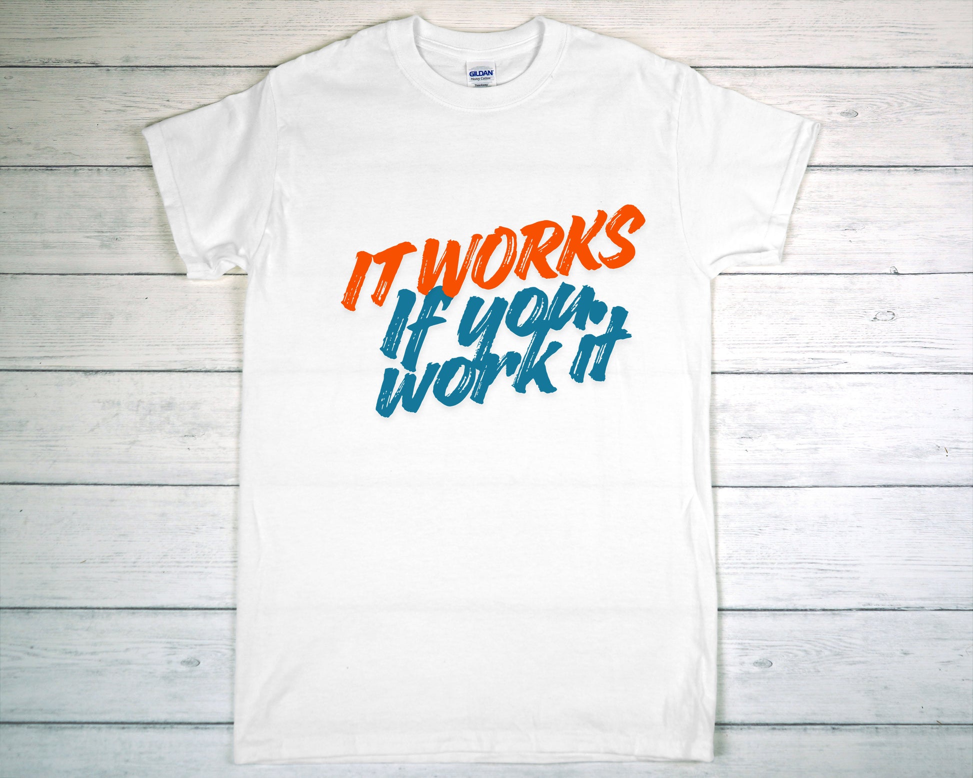 White t-shirt with motivational text 'It works if you work it' on a wooden surface