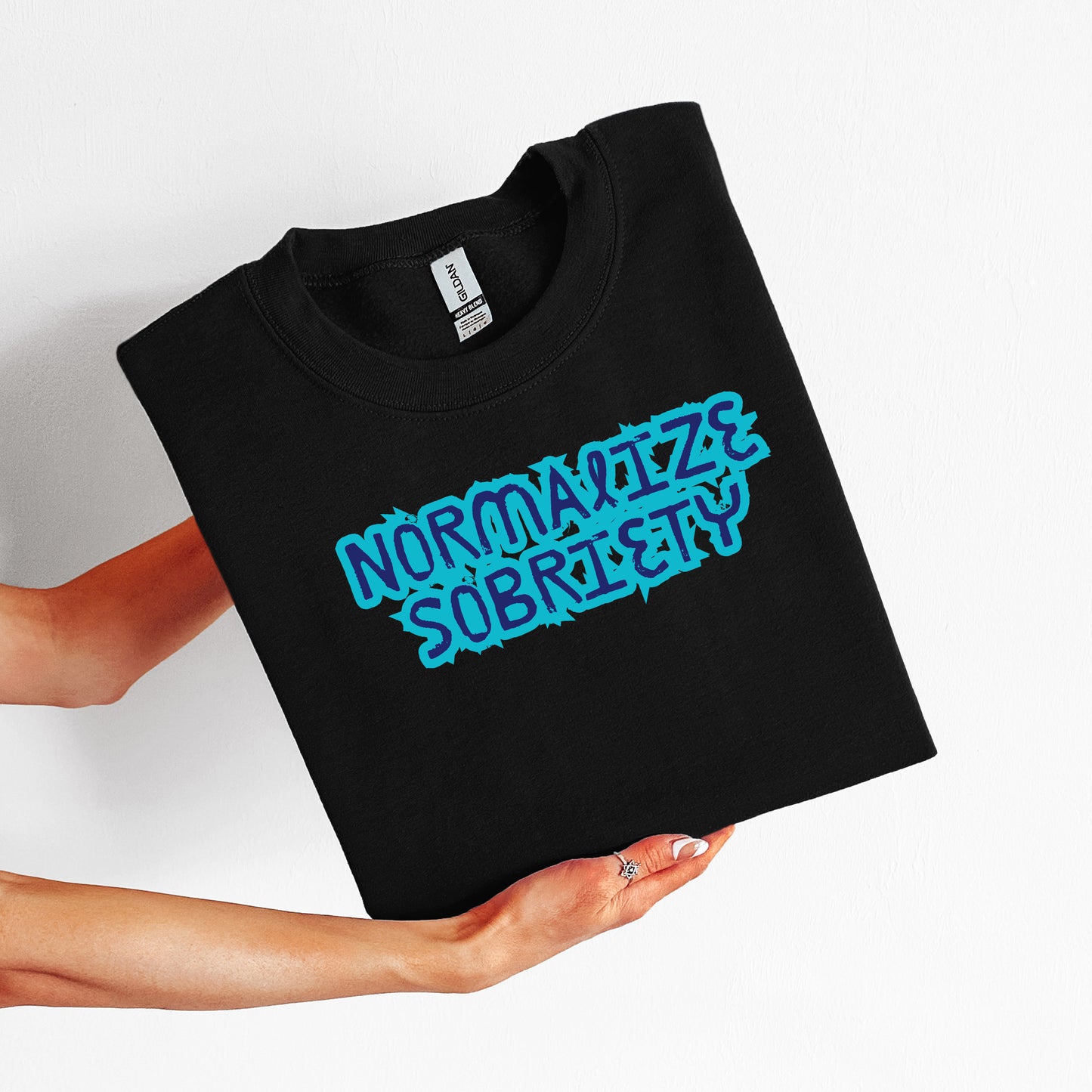 Black t-shirt with blue text "Normalize Sobriety" held by a person on a white background