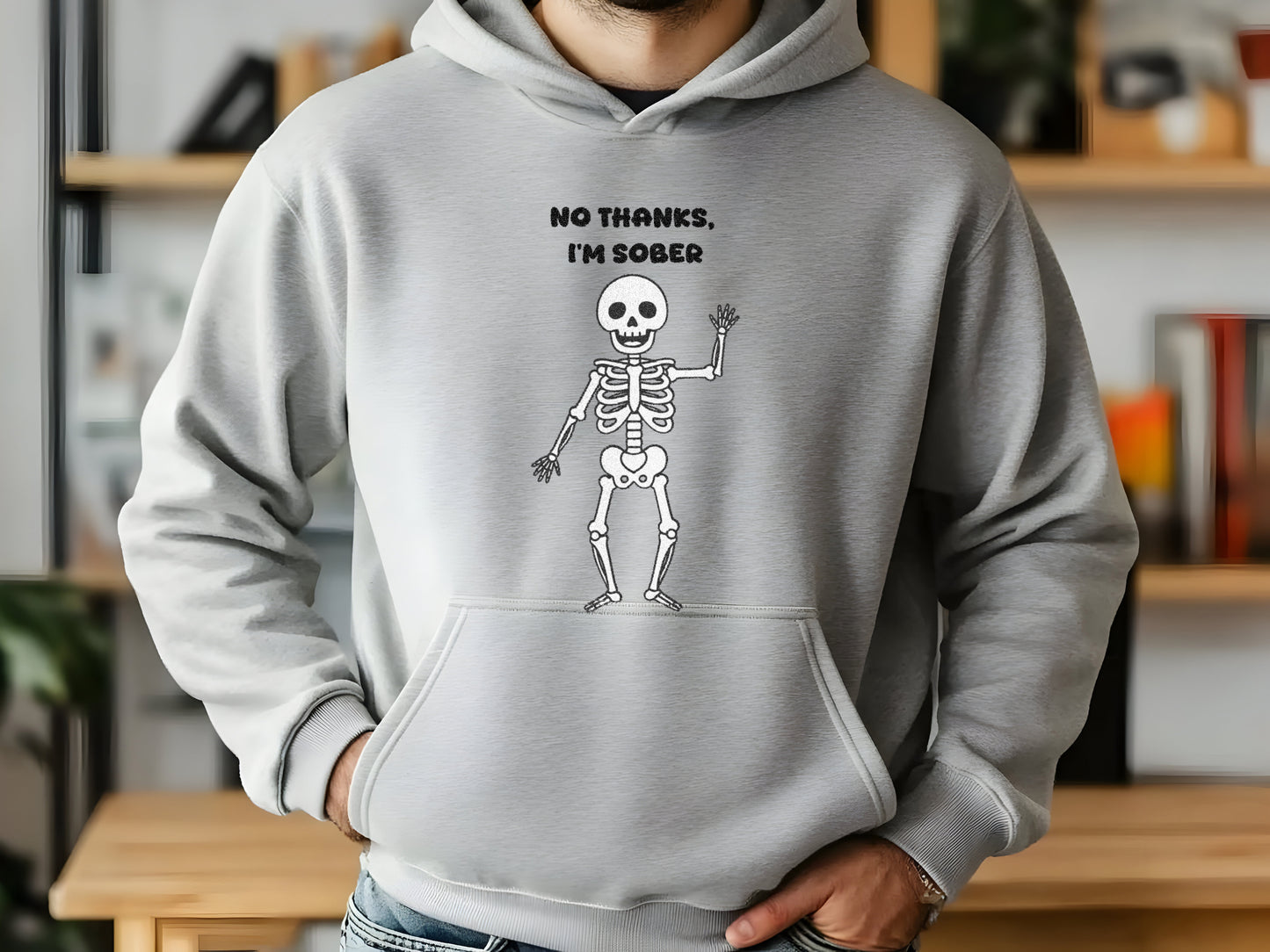 Person wearing a gray hoodie with a skeleton graphic and text 'No Thanks, I'm Sober' in a room.