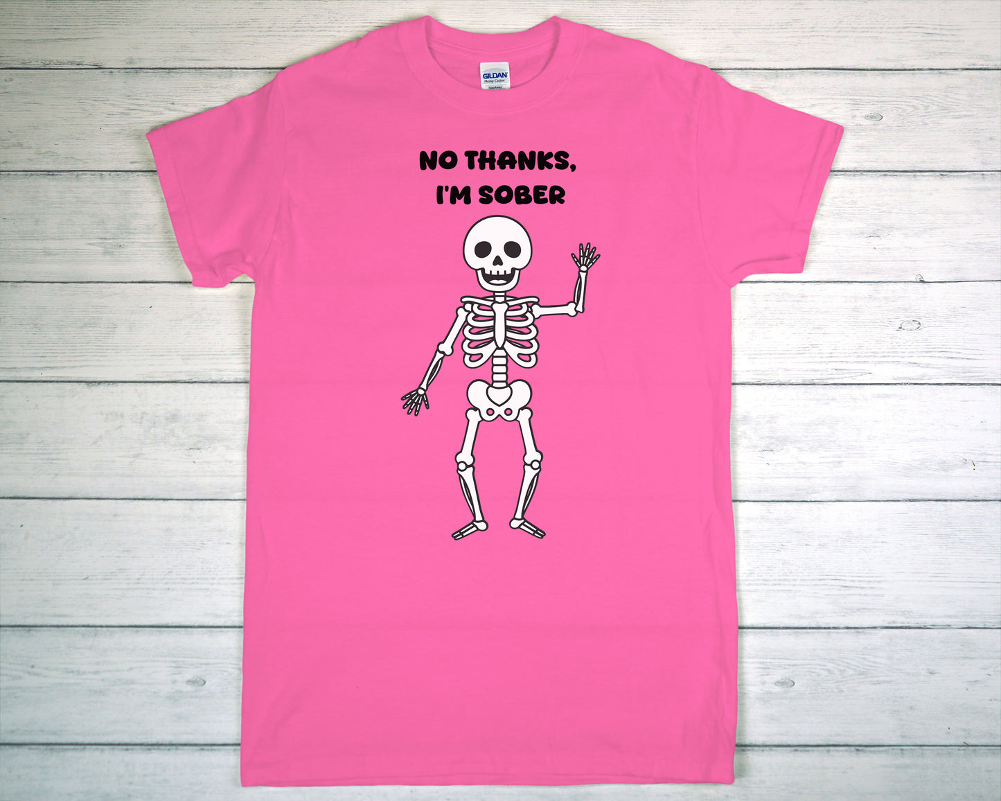 Pink t-shirt with a skeleton graphic and text 'No Thanks, I'm Sober' on a wooden surface.