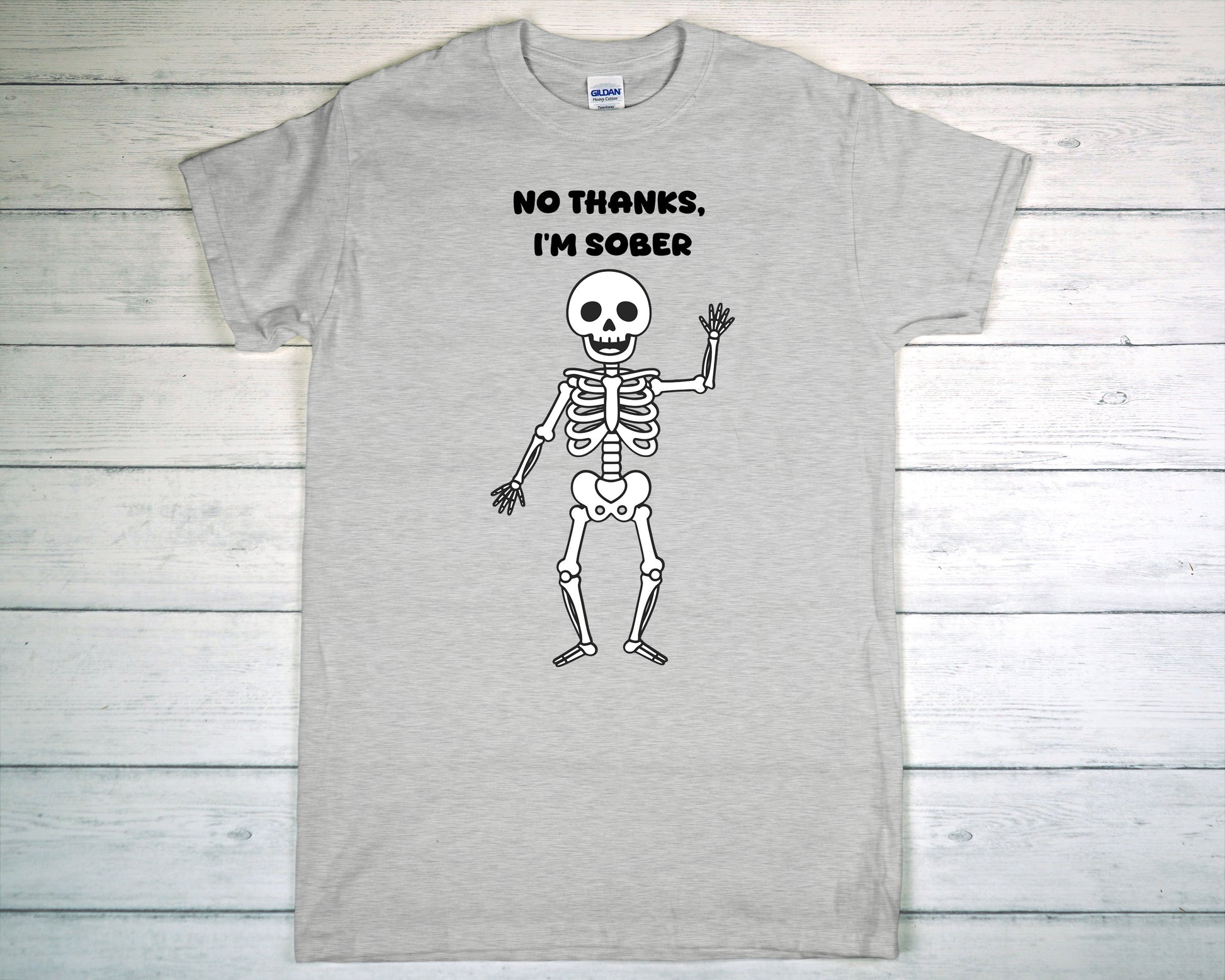 Gray t-shirt with a skeleton graphic and text 'No thanks, I'm sober' on a wooden surface.