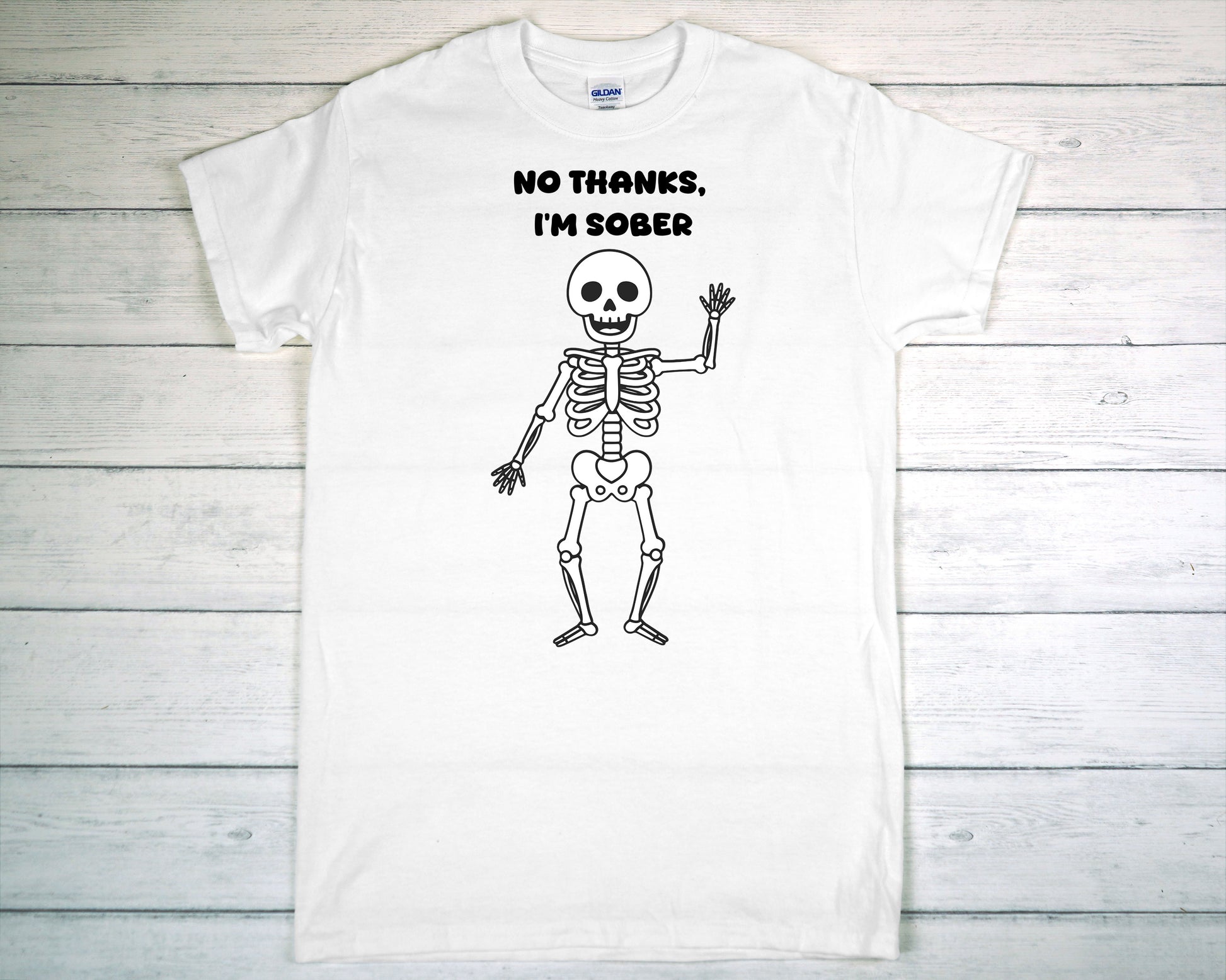 White t-shirt with a skeleton graphic and 'No Thanks, I'm Sober' text on a wooden surface