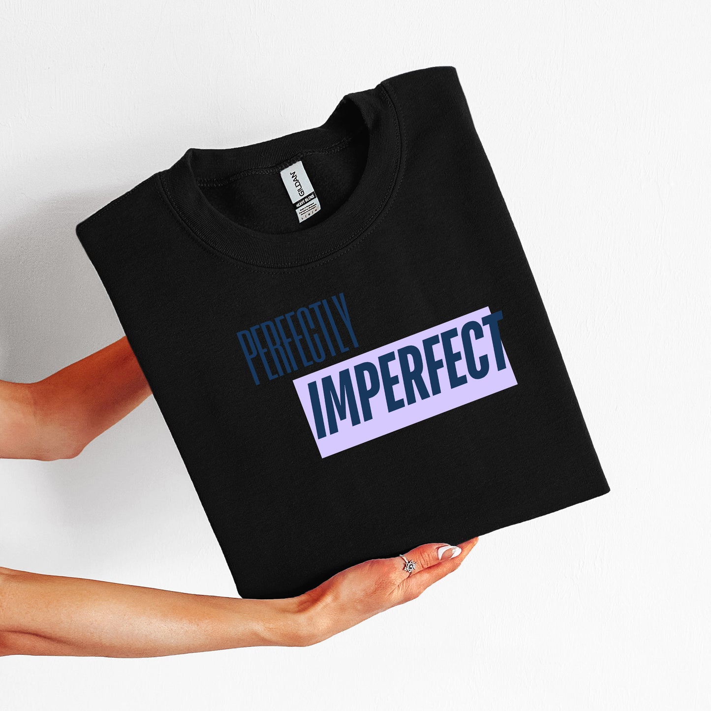 Black t-shirt with 'Perfectly Imperfect' text held by a person on a white background