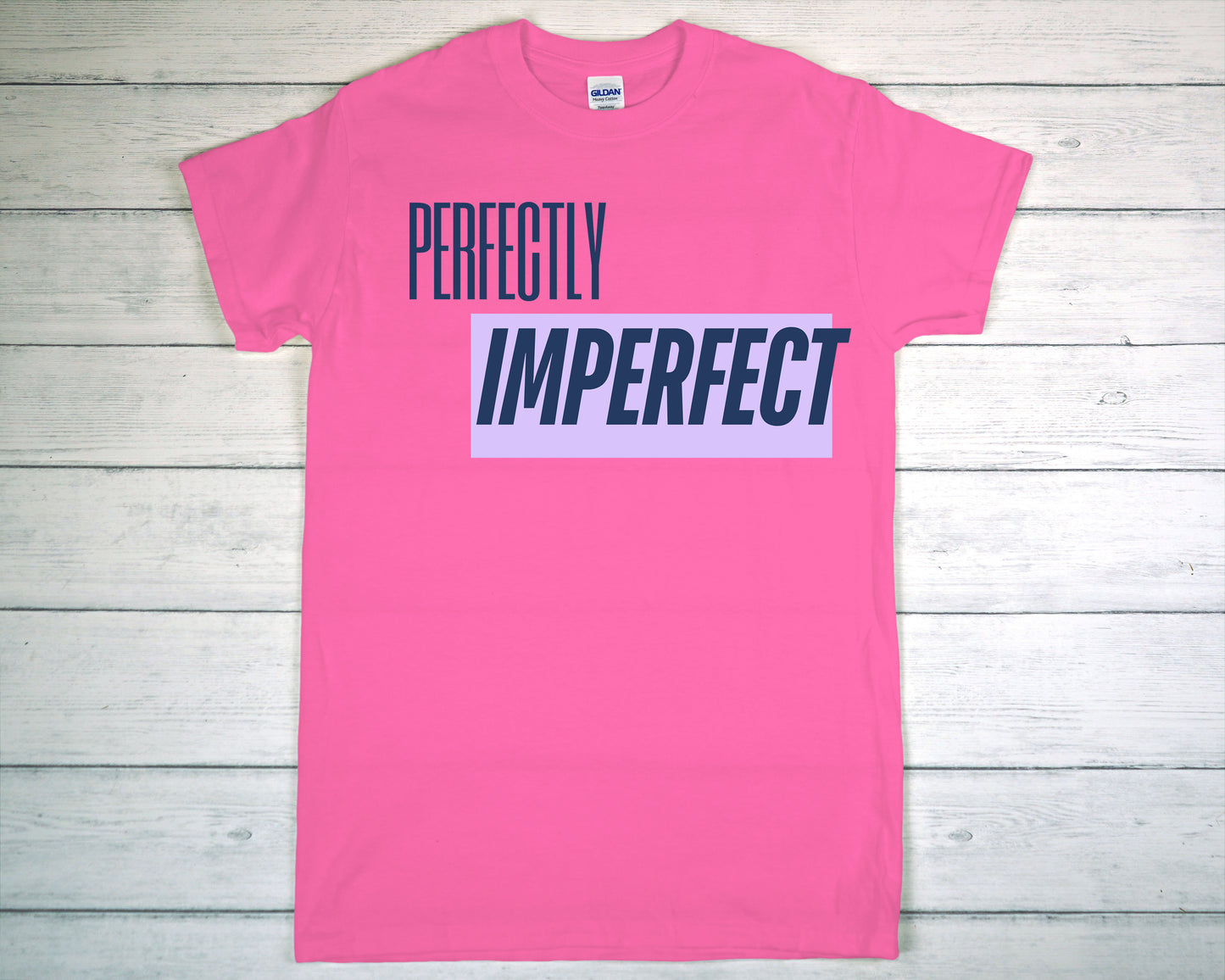 Pink t-shirt with 'Perfectly Imperfect' text on a wooden surface