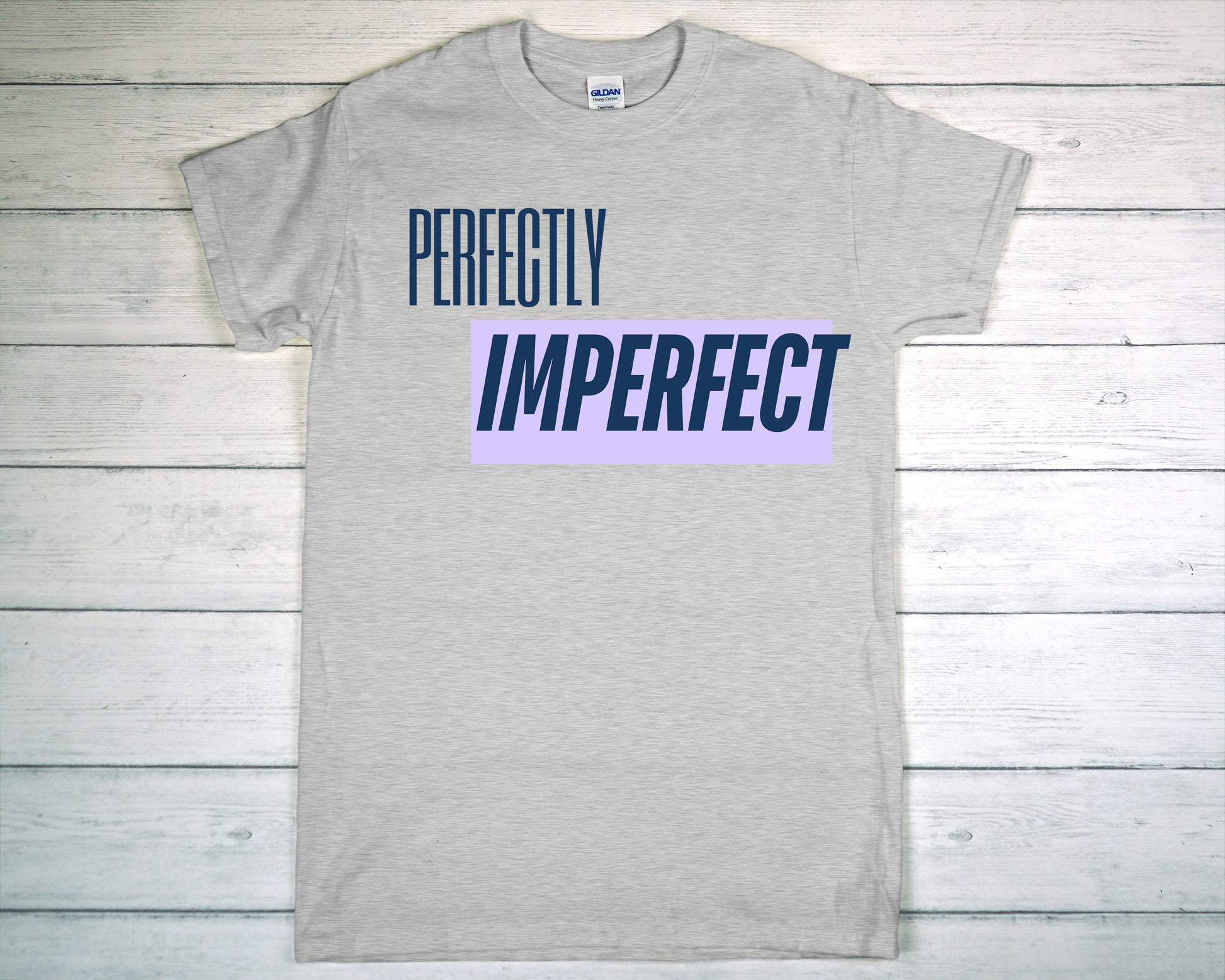 Gray t-shirt with 'PERFECTLY IMPERFECT' text on a wooden surface