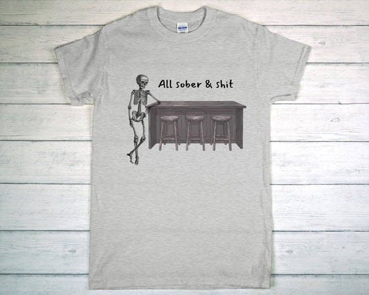 Gray t-shirt with a skeleton and bar graphic and text 'All sober & shit' on a wooden background