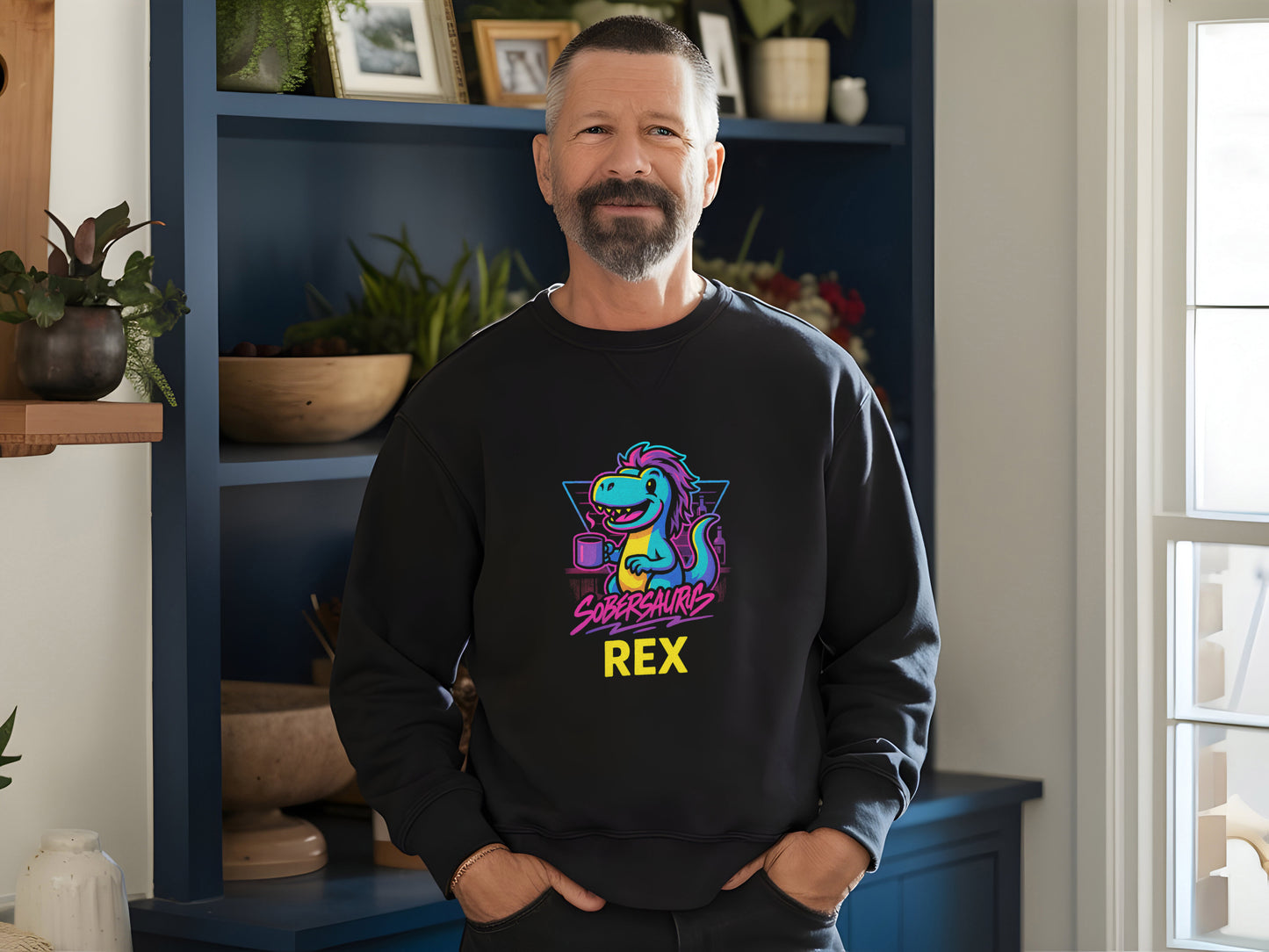 Man wearing a black sweatshirt with a colorful graphic and "Sobersaurus Rex", standing in a room with plants and shelves.