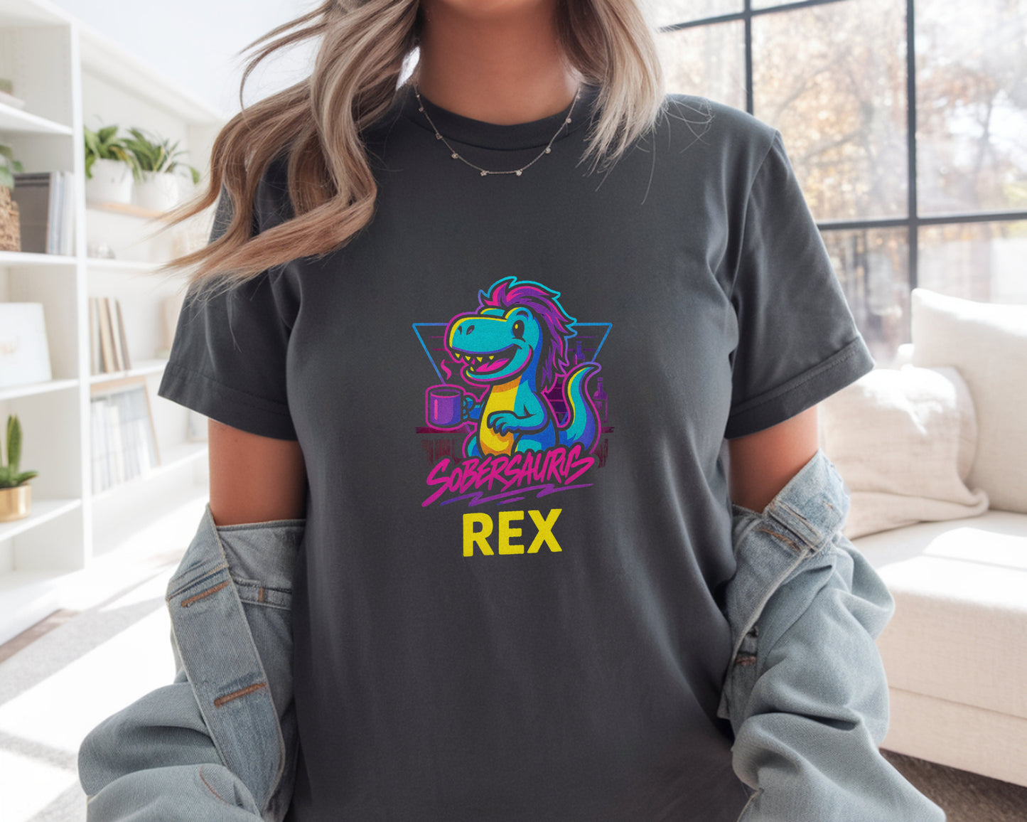 Person wearing a dark gray t-shirt with a colorful dinosaur graphic and "Sobersaurus Rex" in a living room.