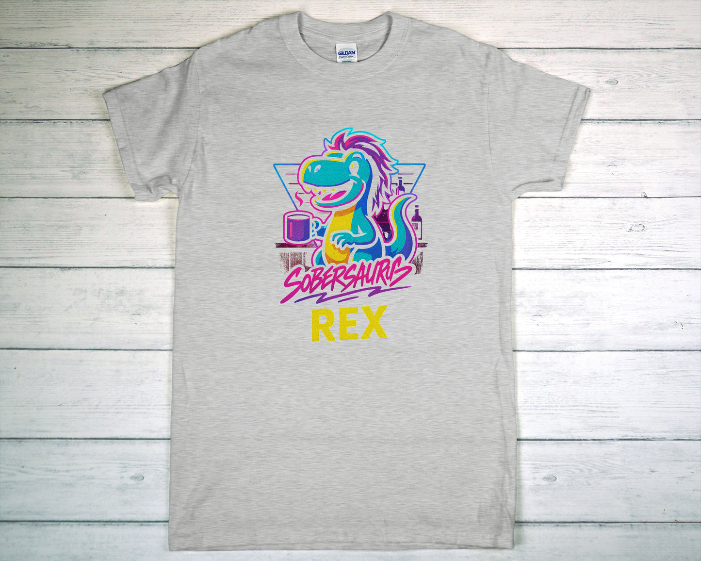 Gray t-shirt with colorful dinosaur graphic and "Sobersaurus Rex" on a wooden surface