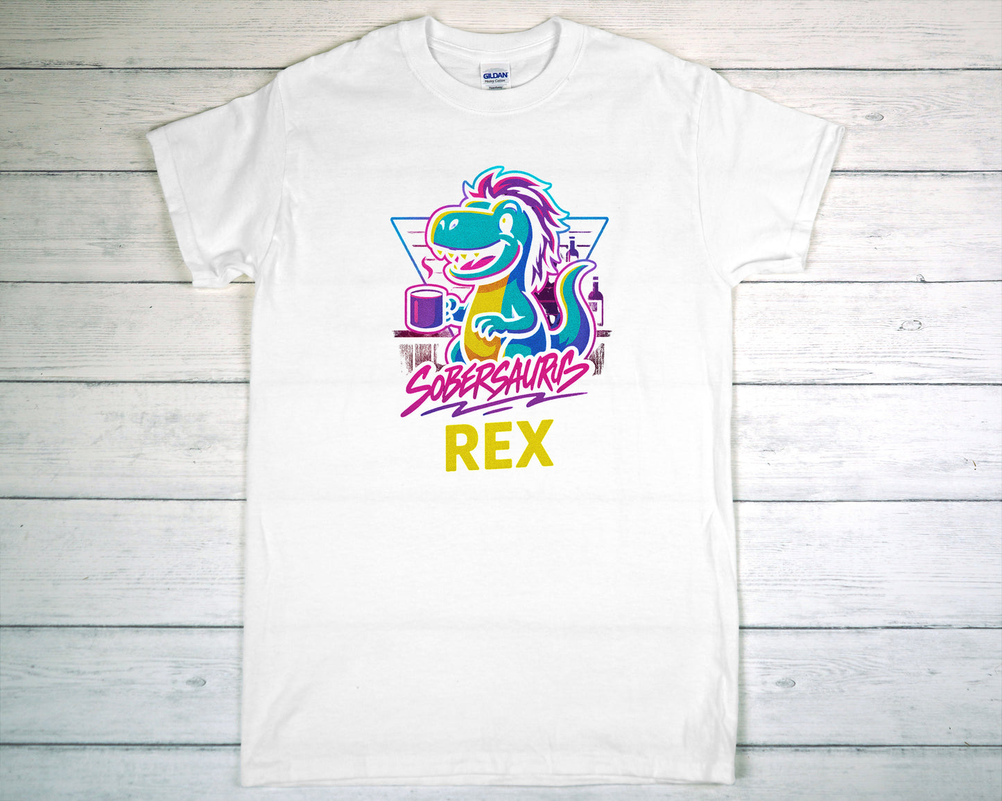 White t-shirt with colorful dinosaur graphic and "Sobersaurus Rex" on a wooden surface