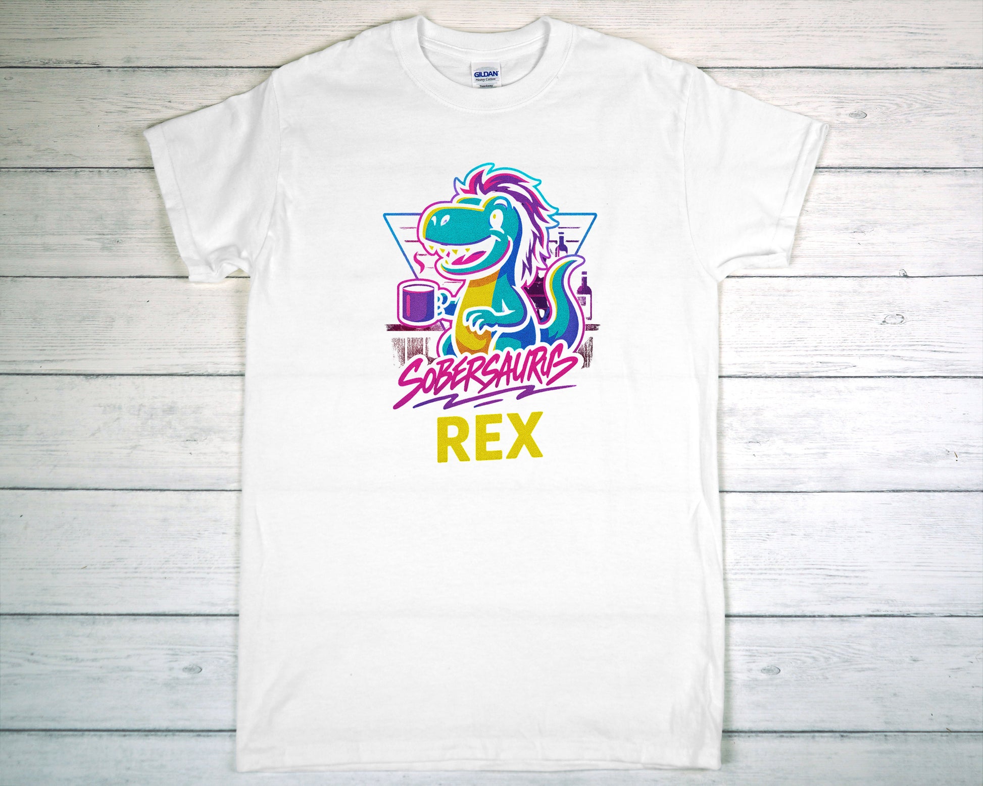 White t-shirt with colorful dinosaur graphic and "Sobersaurus Rex" on a wooden surface